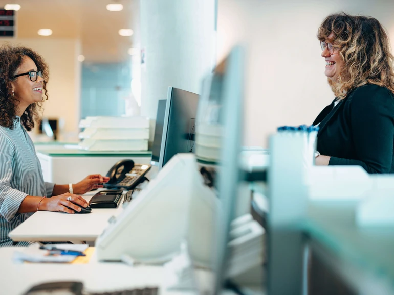 Moderne Bürgerberatung am Empfang Mitarbeiterin am Serviceschalter spricht lächelnd mit einer Besucherin in einem modernen Büro.