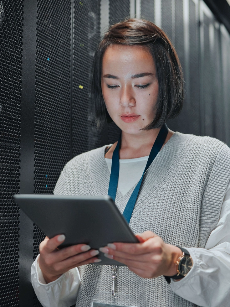 IT-Spezialistin im Rechenzentrum Technikerin arbeitet im Serverraum mit einem Tablet vor hochmodernen Rack-Systemen.