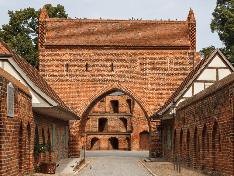 Neubrandenburg – Historisches Stadttor Backsteinernes Stadttor mit spitzem Giebel, flankiert von Fachwerkhäusern in einer historischen Gasse.
