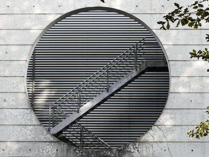 Garching bei München – Moderne Architektur Modernes Gebäude mit kreisförmiger Öffnung und einer diagonalen Metalltreppe vor lamellenartiger Fassade.