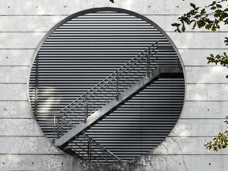 Garching bei München – Moderne Architektur Modernes Gebäude mit kreisförmiger Öffnung und einer diagonalen Metalltreppe vor lamellenartiger Fassade.