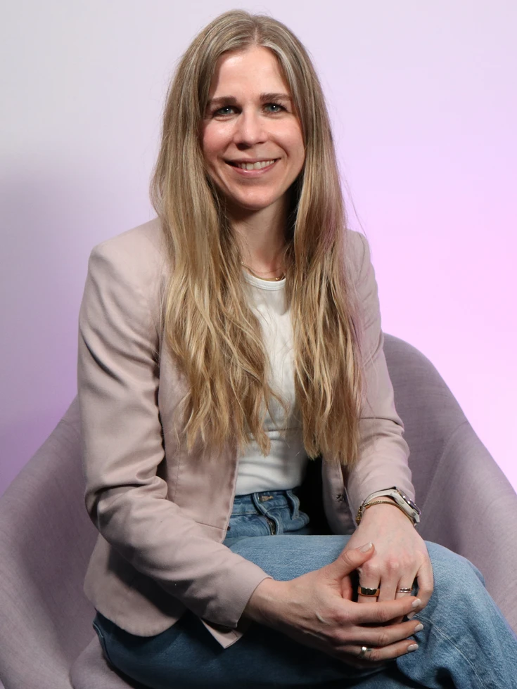 Portrait im Büro - Flexibilität und Verantwortung Portrait einer lächelnden conet Mitarbeiterin in beigem Blazer sitzend in Studio auf hellbraunem Stuhl