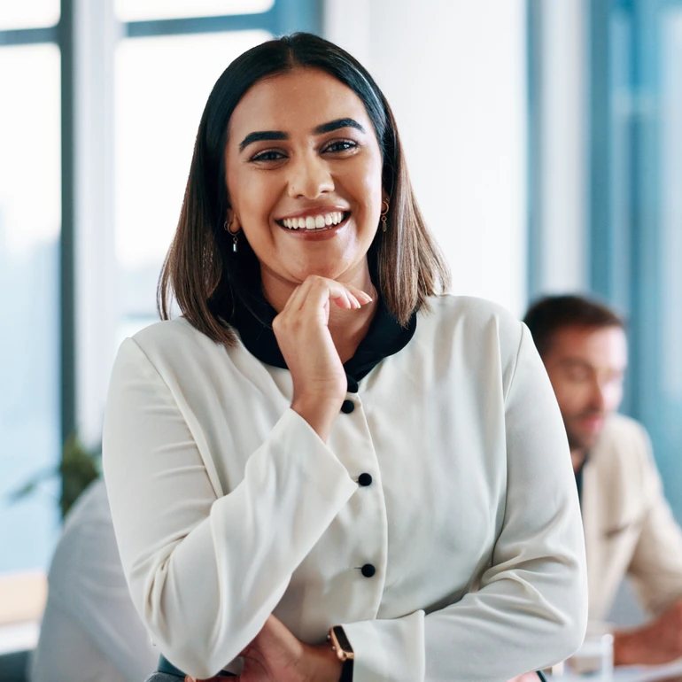Portrait im Büro Frau in weißer Bluse lächelt selbstbewusst mit verschränkten Armen in die Kamera, Büroraum im Hintergrund