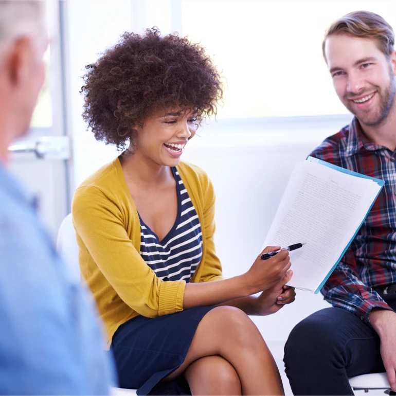 Besprechung im Team Frau in gelbem Cardigan und Mann im karierten Hemd sitzen im Gespräch, die Frau hält ein Dokument in der Hand