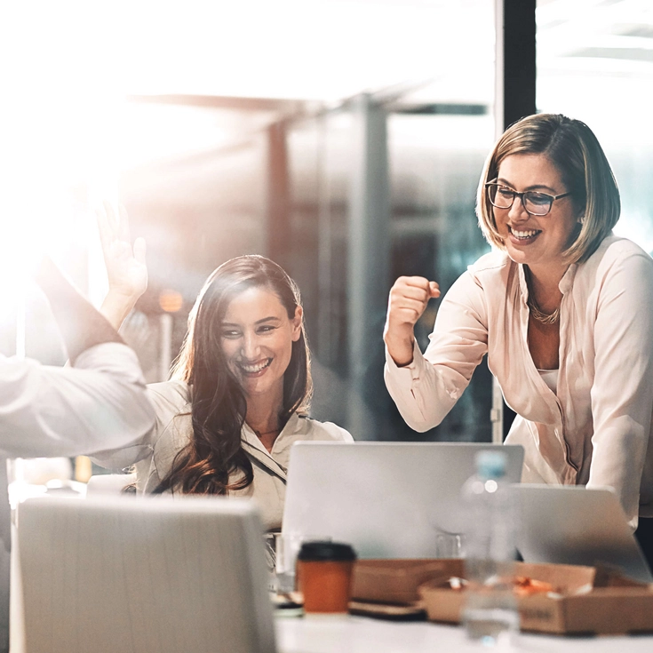 Erfolgreiches Team feiert Projekterfolg Gruppe von Mitarbeitenden jubelt und lacht während eines Meetings in einem modernen Büro.